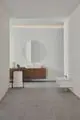 Waschtisch mit integrierter Armatur von Ideal Standard, suspendiert, in minimalistischer Gestaltung, kombiniert mit einem runden Spiegel und einer Holzkommode in einem modernen Badezimmer.